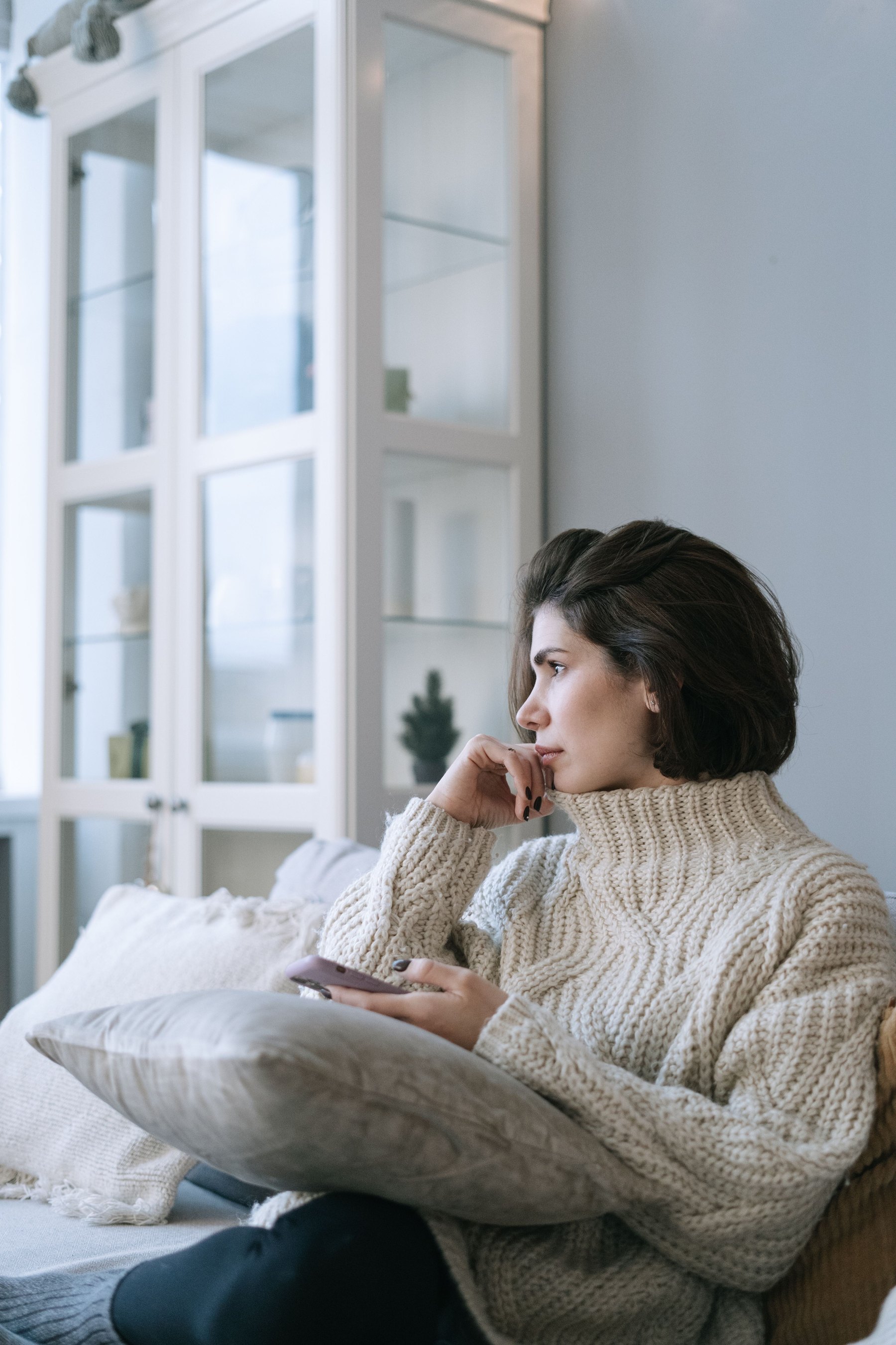 Adult sitting thoughtfully on a sofa in a calm living room setting